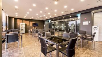 A modern conference room with glass tables and chairs, a large screen, and a refrigerator.