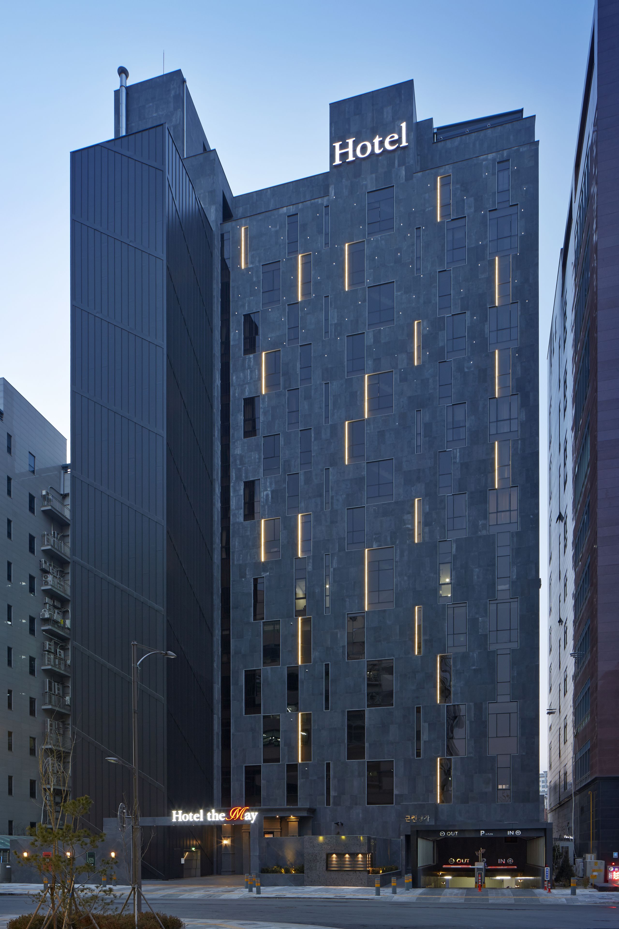 A modern hotel building with a prominent 'Hotel' sign at the top, featuring a unique geometric facade with illuminated windows.