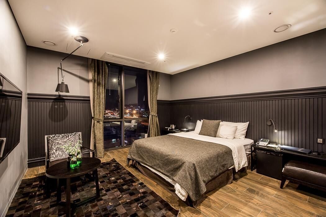 Une chambre d’hôtel moderne avec un grand lit, un bureau et une chaise. La fenêtre offre une vue sur la ville.