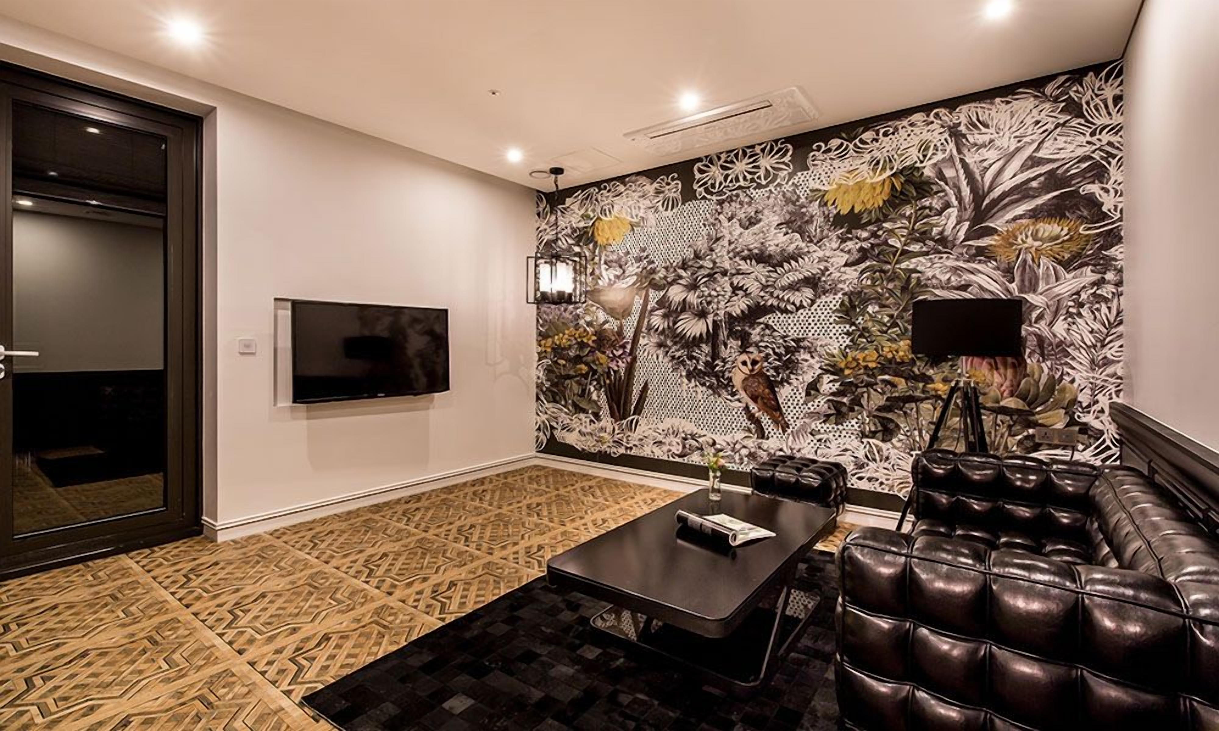 Una habitación moderna con alfombra estampada, un sofá de cuero negro, una mesa de comedor y un televisor montado en la pared.