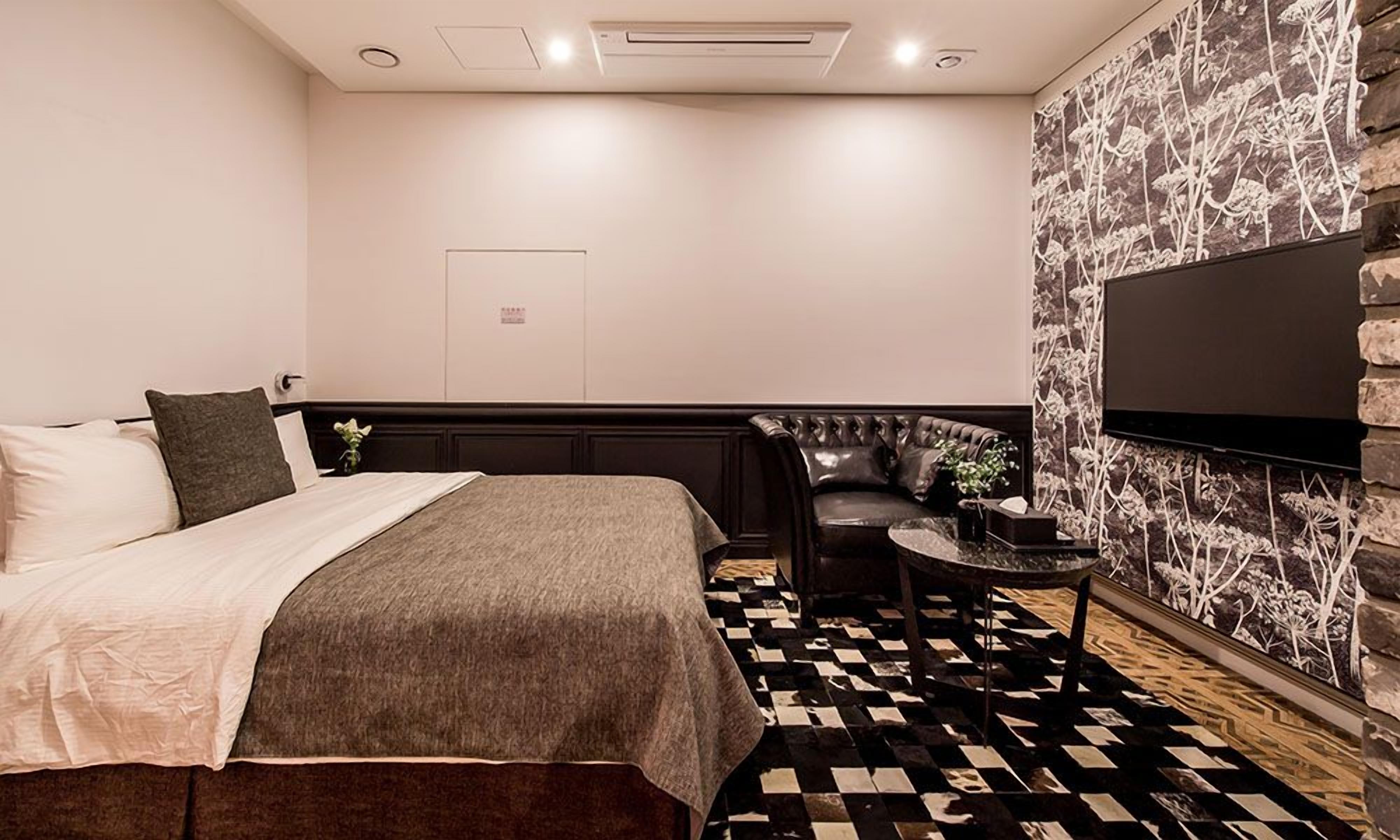 A hotel room with a bed, a seating area, a TV, and a patterned wall.