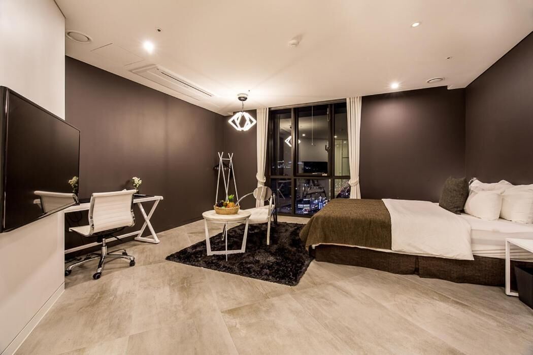 A modern hotel room with a bed, desk, chair, and a city view through the window.
