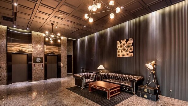 A lobby with a leather sofa, a coffee table, a lamp, and a wall with a decorative piece. - Hotel the May (Namyangju)