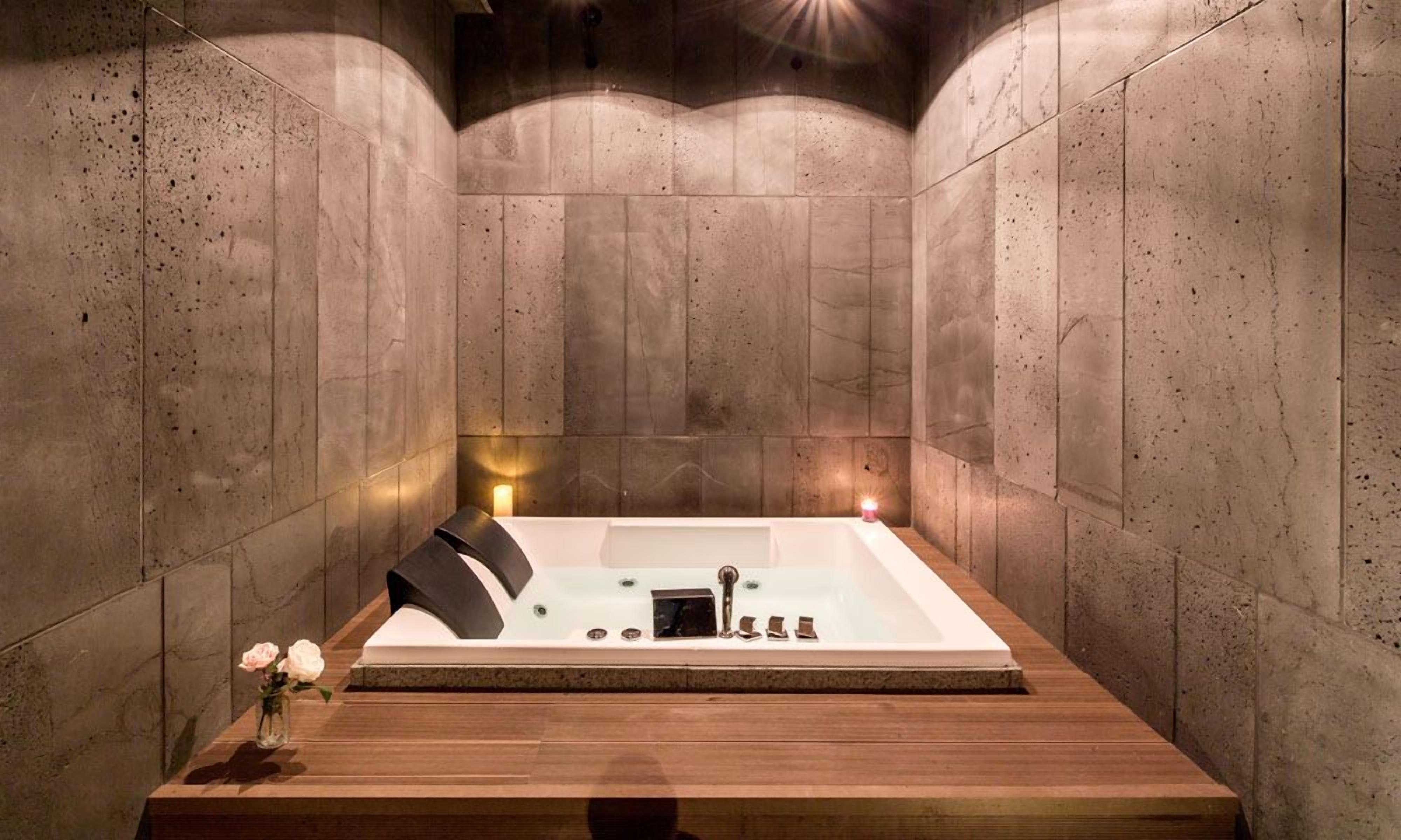 A modern bathroom with a freestanding bathtub, wooden floor, and stone walls.