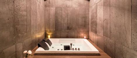A modern bathroom with a freestanding bathtub, wooden floor, and stone walls.