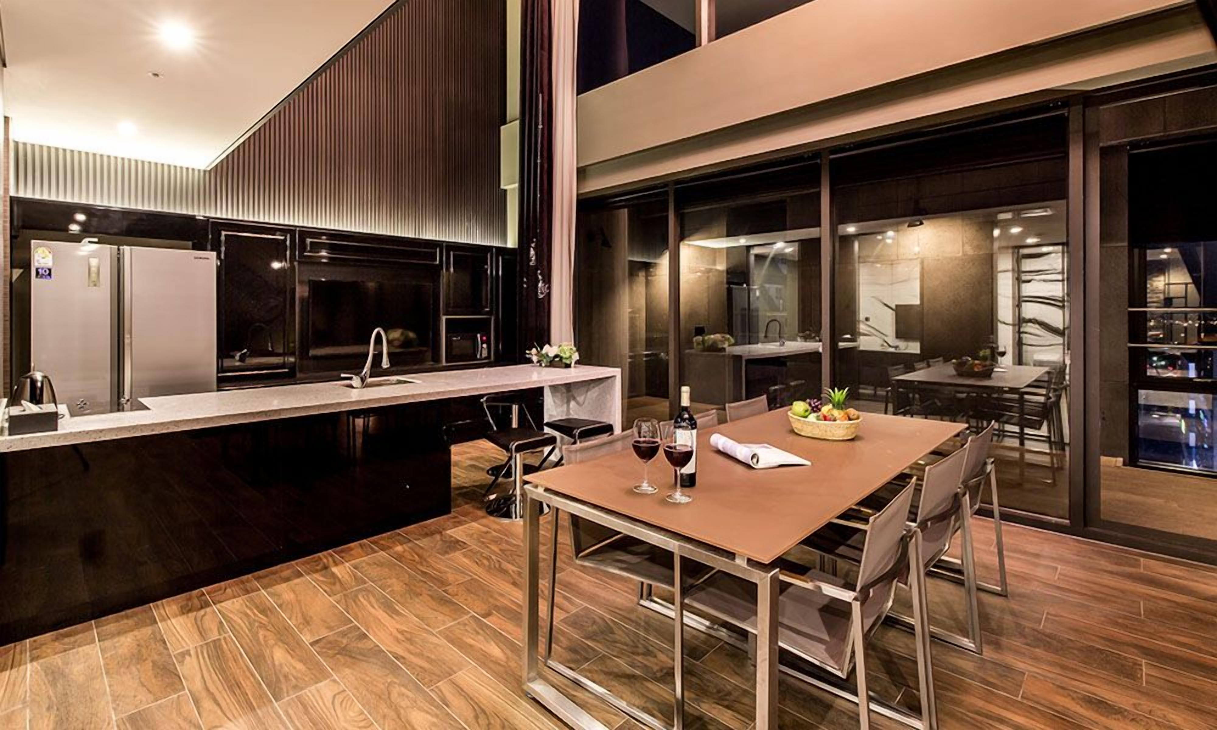A modern kitchen with a dining area, featuring a large island, stainless steel appliances, and a view of the city at night.