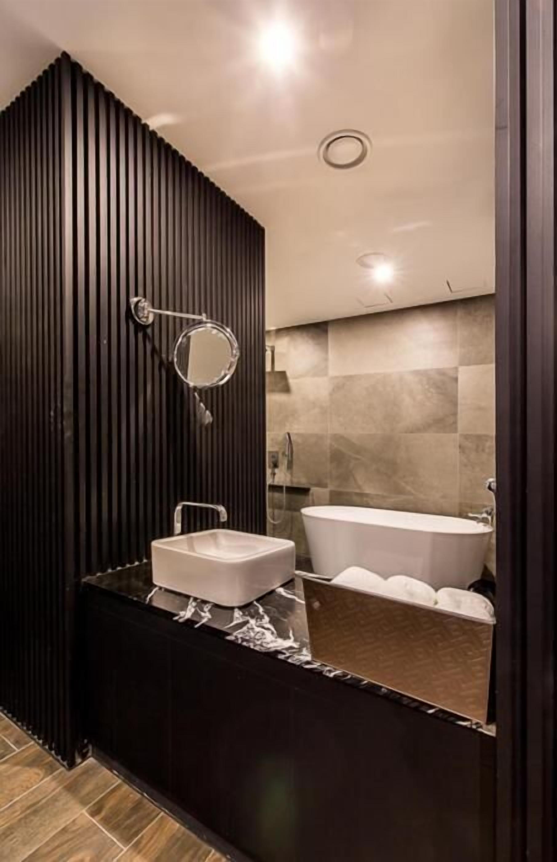 Une salle de bain moderne avec un mur recouvert de panneaux en bois foncé, un lavabo blanc, un grand miroir et une baignoire sur pieds.