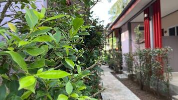 Un sendero bordeado de vegetación y un edificio con pilares rojos.