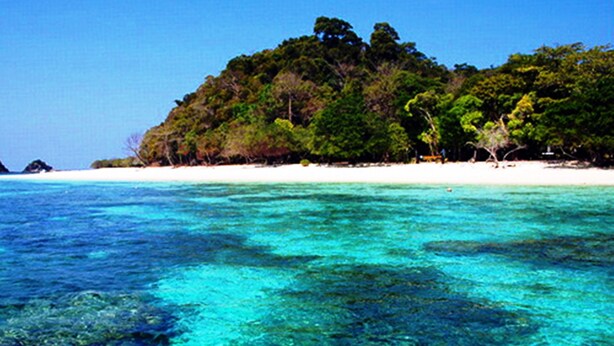 Uma praia com águas turquesa cristalinas, uma orla arenosa e uma colina coberta por floresta.