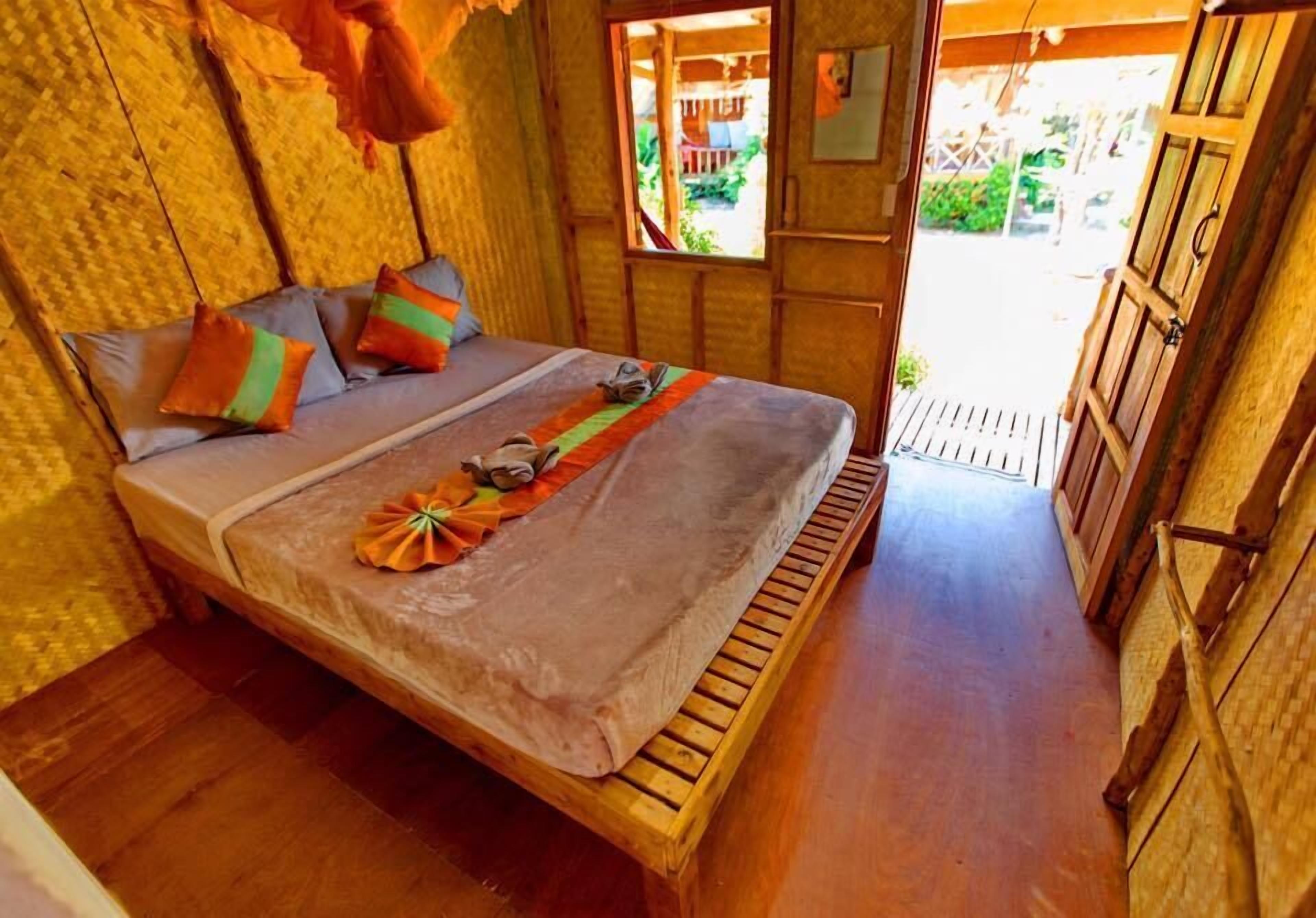 Un lit avec un cadre en bois et une couvre-lit grise, des oreillers à rayures orange et vertes, et un petit objet décoratif posé sur le lit.