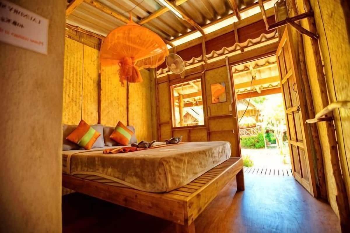 A room with a wooden bed, a hanging mosquito net, and a view of the outside.
