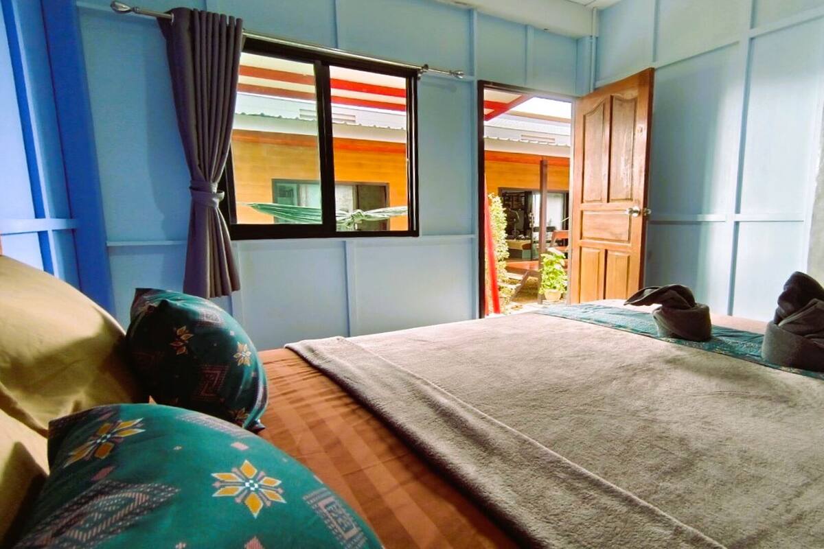 A bedroom with a bed, pillows, a window, and a view of the outside.
