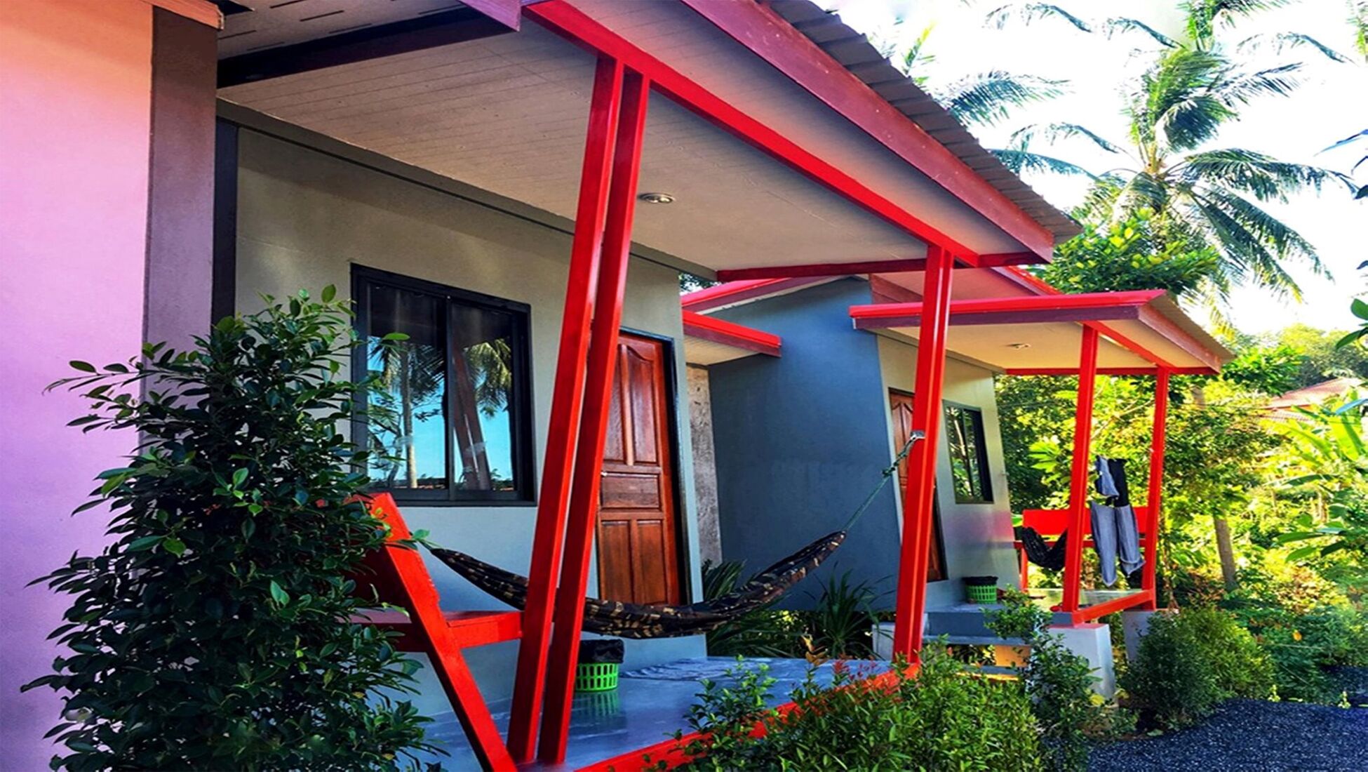 A modern house with a red and grey color scheme, a large window, and a hammock on the porch.