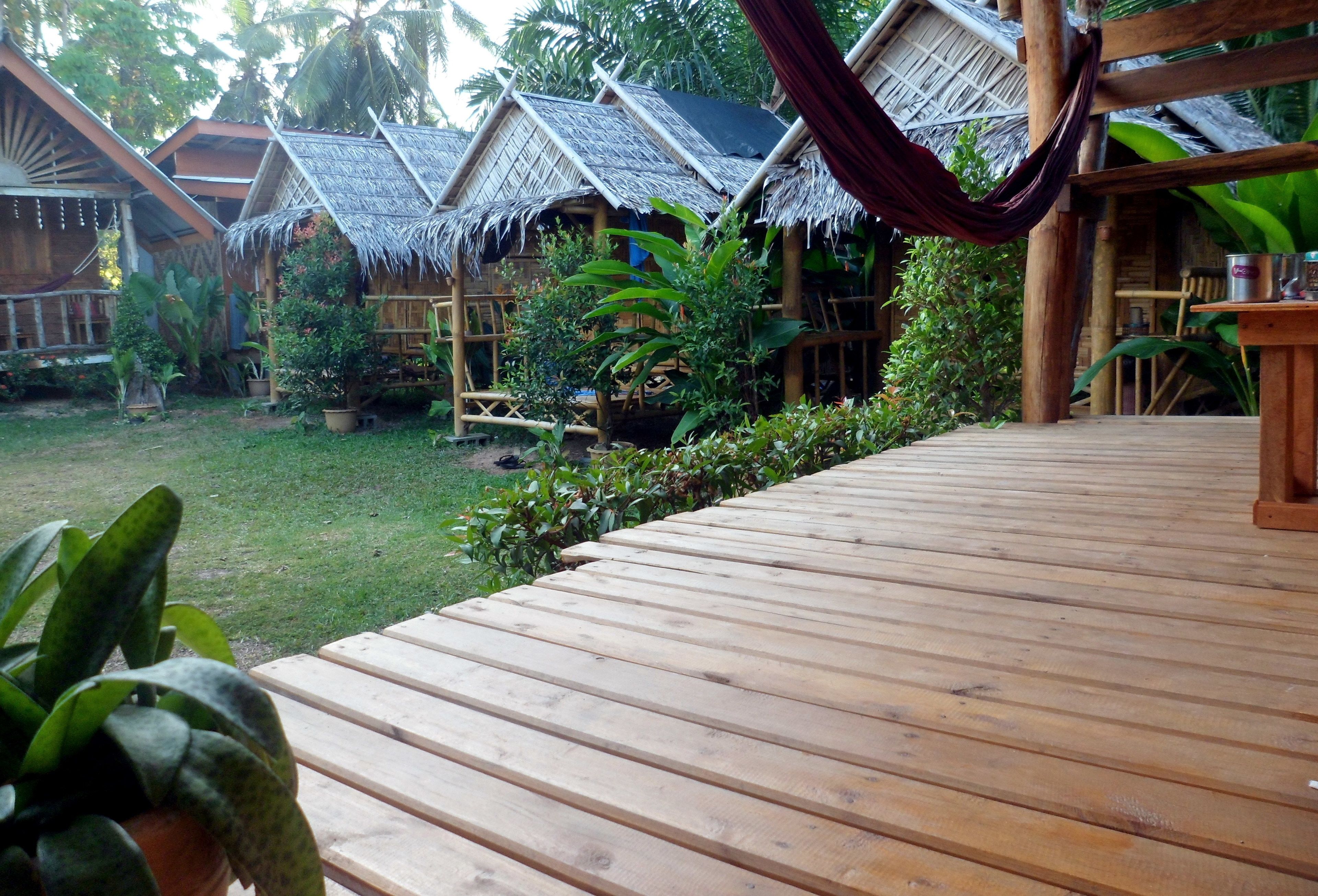 Una terraza de madera que conduce a cabañas con techo de paja, rodeadas de exuberante vegetación.