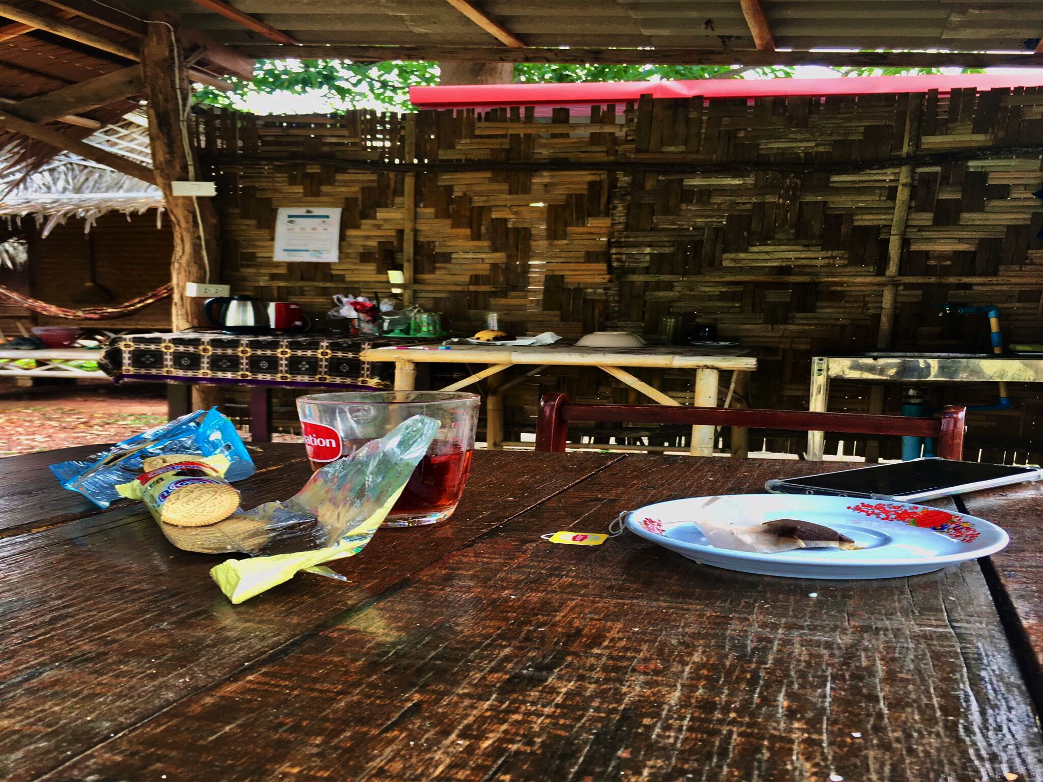 Una mesa de madera rústica con un vaso de plástico, un vaso de líquido rojo y un plato con una cuchara.