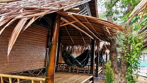 Uma cabana de bambu com uma rede, cercada por árvores e vegetação.
