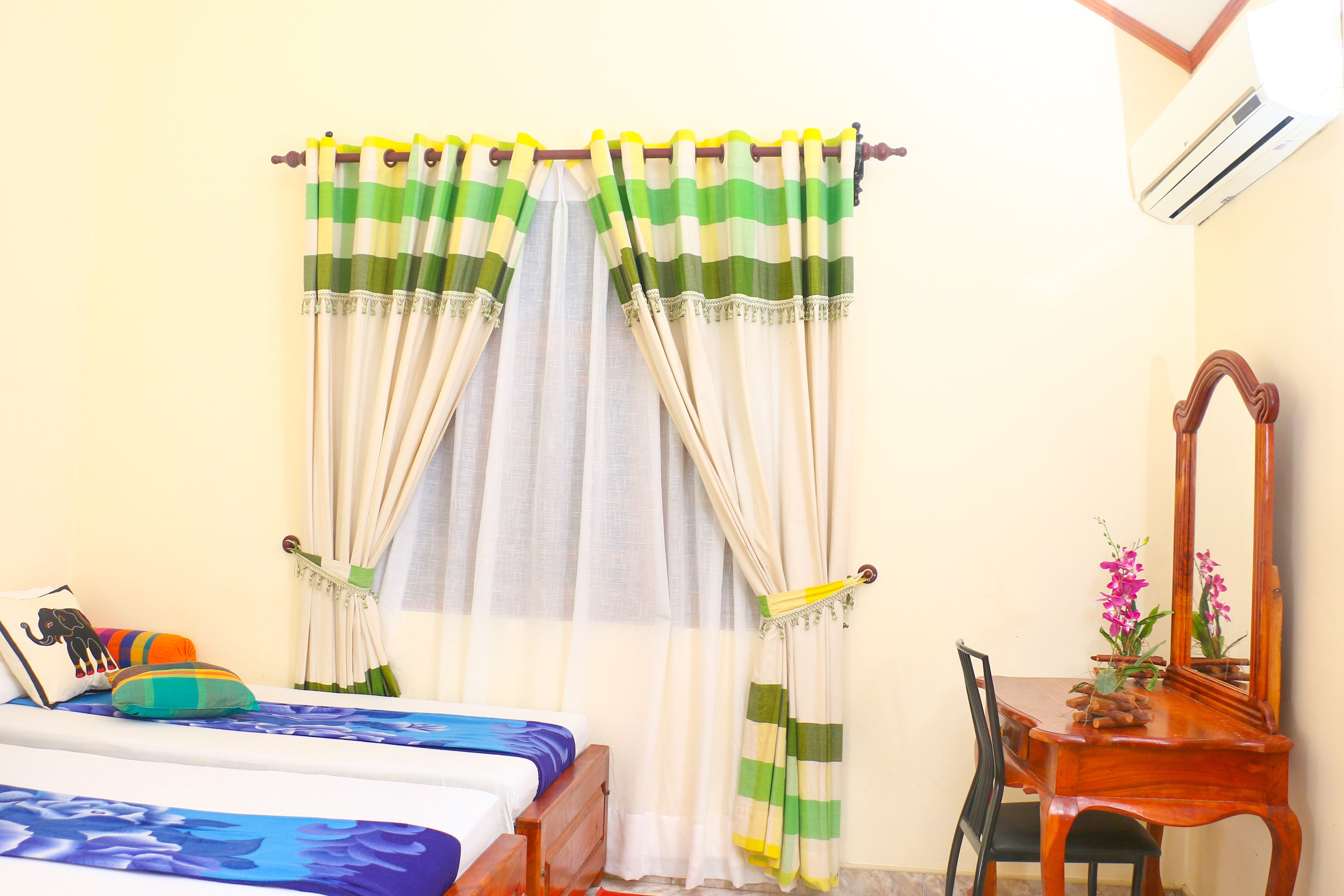A bedroom with a bed, a wooden dresser, a mirror, and curtains.