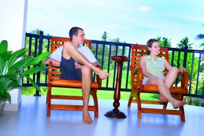 Two people sitting on wooden chairs on a balcony with a view of greenery and a fence. - Nature Resort Tissamaharama (Thissamaharama)