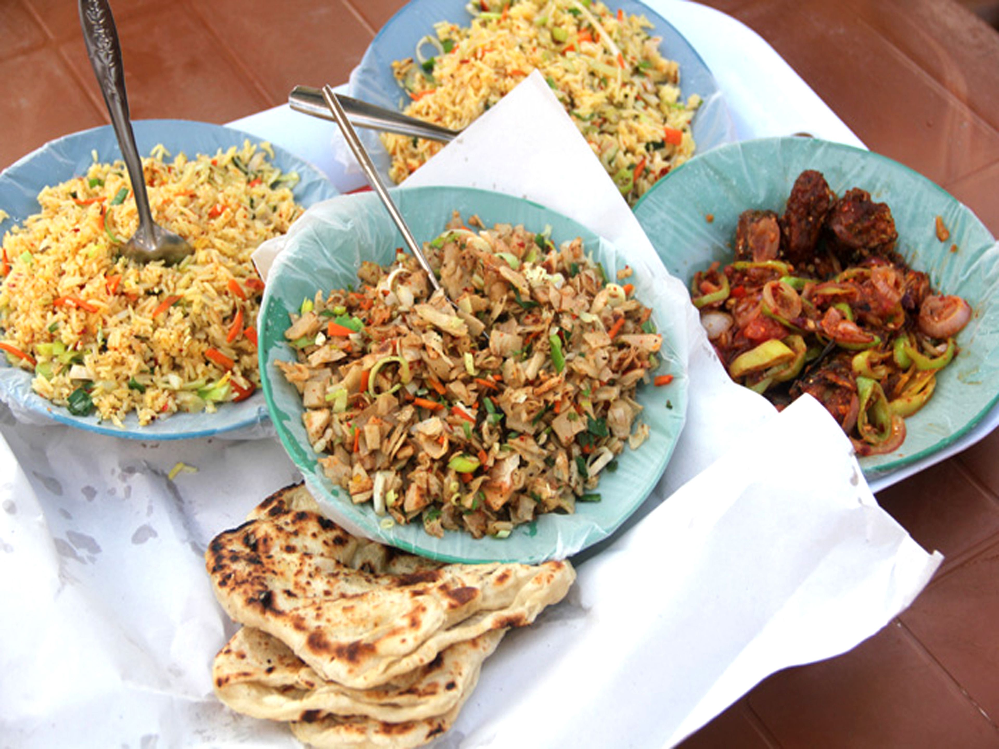 A table with various dishes, including rice, stir-fried vegetables, and meat, along with flatbreads.