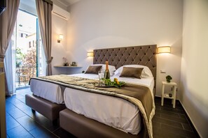 A hotel room with a large bed, a bench, a bedside table, and a view of the outside balcony.