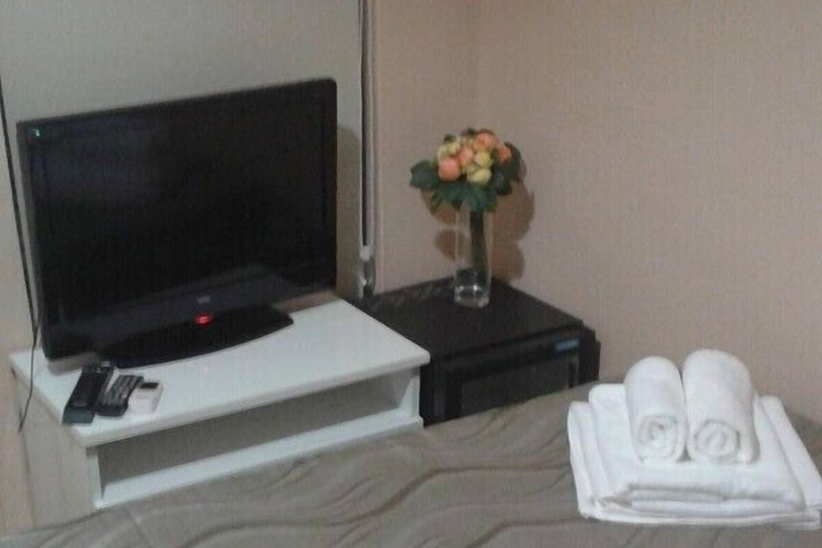 A hotel room with a bed, a TV, a vase with flowers, and a tray with towels.