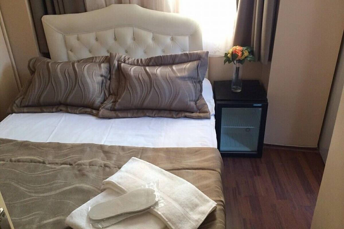 A neatly made bed with a white comforter and two patterned pillows, a bedside table with a vase of flowers, and a small black nightstand.