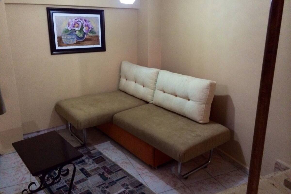 A room with a beige sofa, a small table, and a framed picture on the wall.