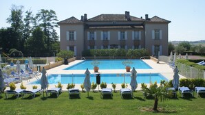 Ein großes Gebäude mit Schwimmbad, umgeben von Liegestühlen und Sonnenschirmen.