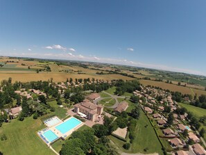 An aerial view of a residential area with a large swimming pool, surrounded by houses and green fields. - Château de Barbet (Lombez)