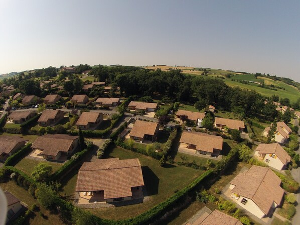 An aerial view of a residential area with houses having similar architecture and layout, surrounded by greenery and hills in the background. - Château de Barbet (Lombez)