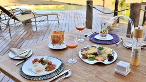 A wooden deck with a table set for breakfast, including plates of food, drinks, and a salt shaker.