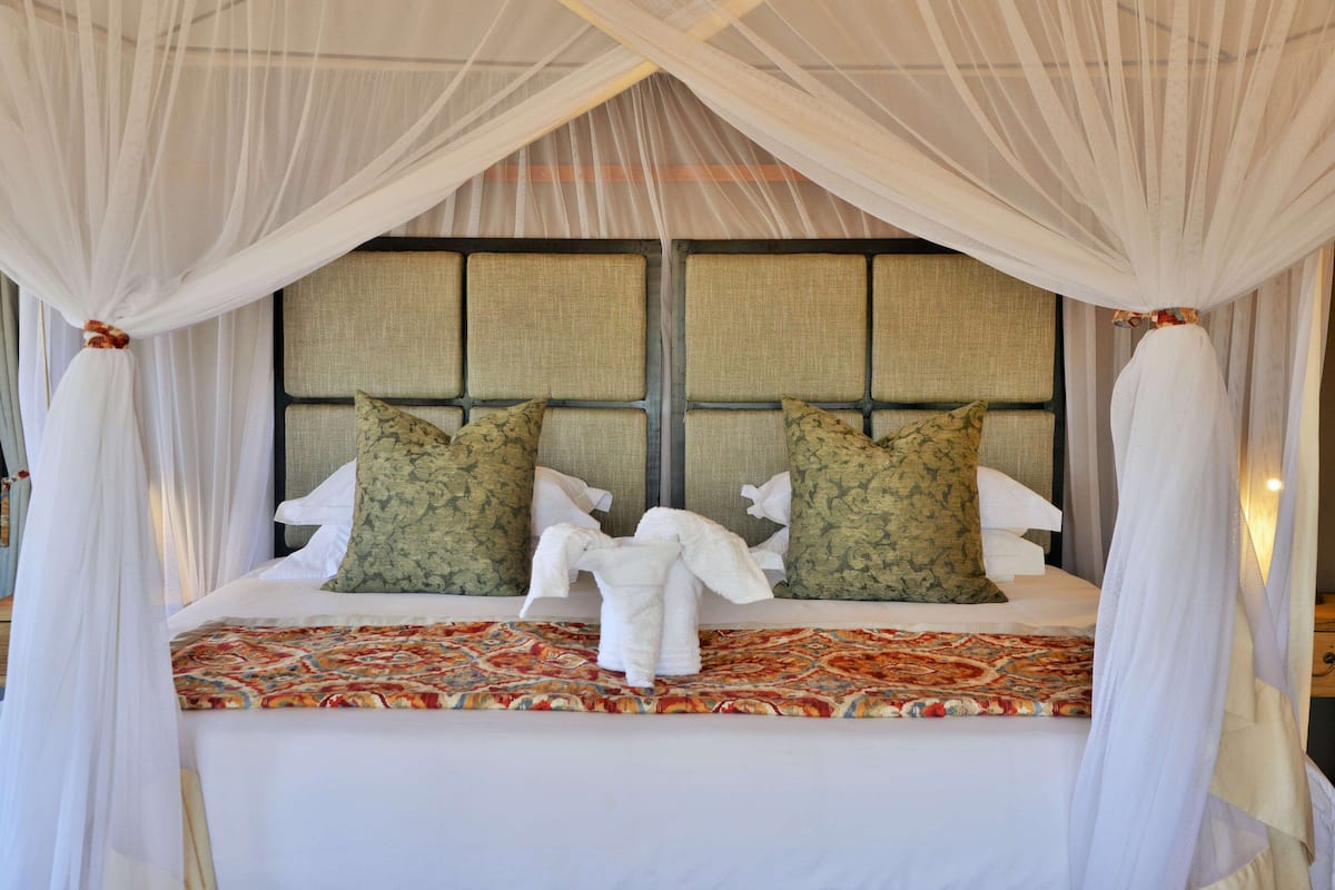 A bed with a canopy, two pillows, and a decorative pillow on a patterned bedspread.