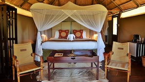 A room with a bed under a canopy, two chairs, a table, and a thatched roof ceiling.