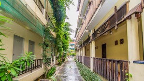 Un étroit sentier, humide, bordé de bâtiments dotés de balcons et de plantes.