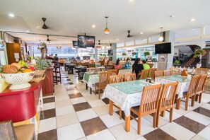 Een restaurant met geruit vloerkleed, houten tafels met bloemenlinnen en een toonbank met fruitpresentatie.