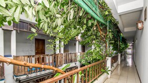 Un couloir doté d’une rambarde en bois, d’un sol carrelé et de plantes vertes qui poussent le long des murs.
