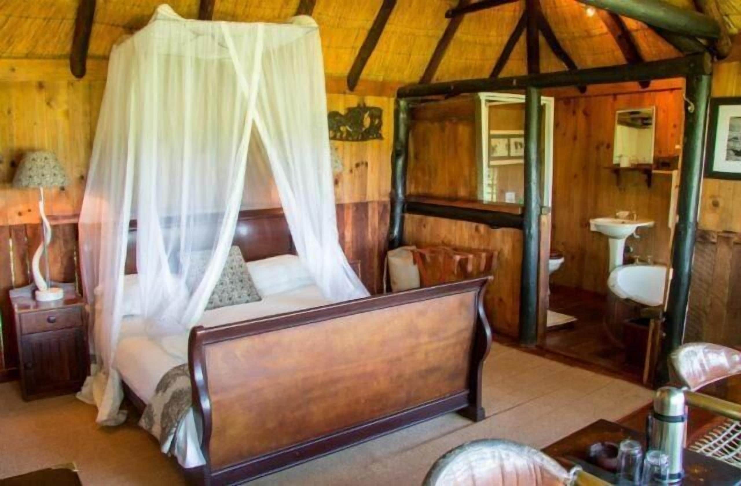 Ein Zimmer mit Holzboden, einem Bett, einem Nachttisch, einem Spiegel, einem Waschbecken und einem Sessel.