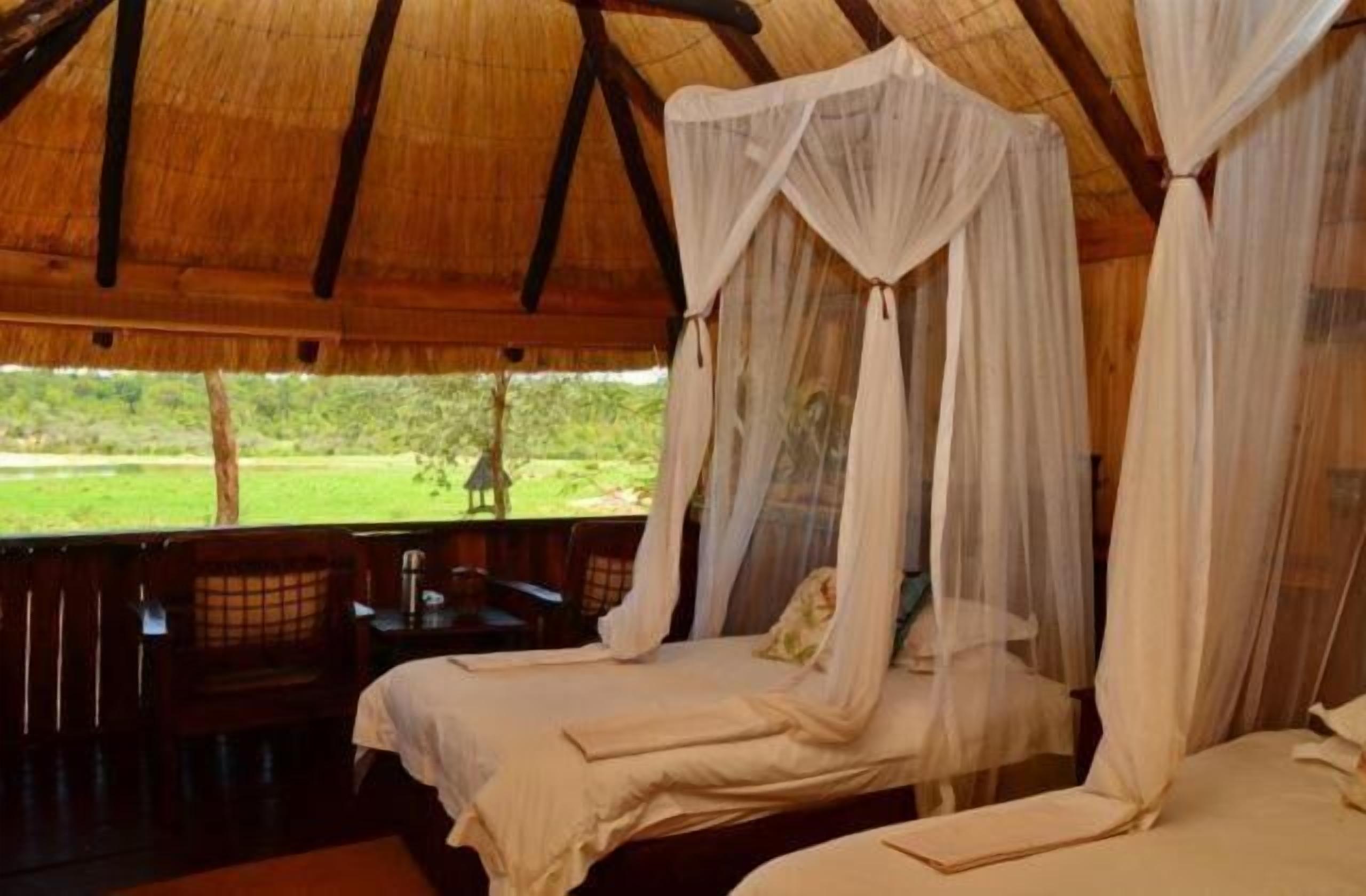A room with two beds, each with a canopy. There is a bench and a table outside the room.