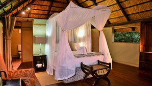 A bedroom with a four-poster bed, a nightstand with a lamp, a chair, and a view of greenery outside. - Ivory Lodge (Dete)