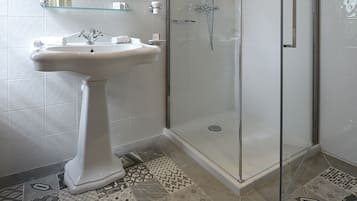 Un baño moderno con ducha de vidrio, lavamanos pedestal y espejo con marco decorativo.