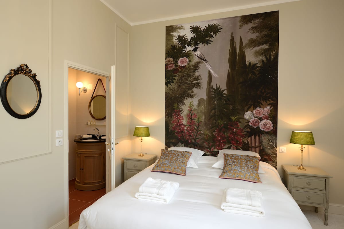 Une chambre d’hôtel avec un grand lit, deux tables de chevet avec des lampes, une armoire en bois et un grand tableau représentant des fleurs accroché au mur.