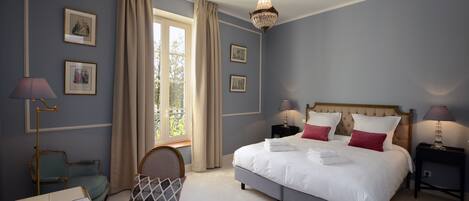 A bedroom with a large bed, a chair, a desk, and a window with curtains.