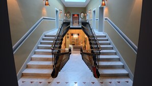 Un magnifique escalier avec une verrière, des marches en marbre et des luminaires fixés au mur.