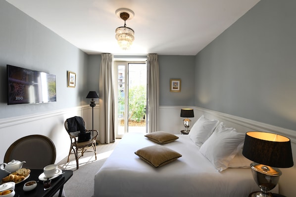 A hotel room with a bed, a television, a dining table with breakfast items, a chair, and a window with curtains. - Grand Hotel Henri - Teritoria (L'Isle-sur-la-Sorgue)