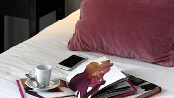 A neatly made bed with a white and pink pillow, a bedside table with a lamp, a book, and a cup with a spoon.