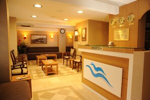 A reception area with a wooden reception desk, multiple seating options including a sofa and chairs, a clock on the wall, and framed artwork. - Deniz Palace Hotel (Istanbul)