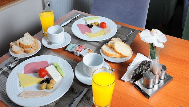 A breakfast table with plates of food, a glass of orange juice, and a view of a cityscape through large windows. - Deniz Palace Hotel (Istanbul)