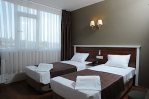 A hotel room with two beds, a wooden headboard, a window with curtains, and a wall-mounted lamp. - Deniz Palace Hotel (Istanbul)