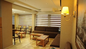 A hotel lobby with a sofa, chairs, tables, and a large window with blinds. - Deniz Palace Hotel (Istanbul)