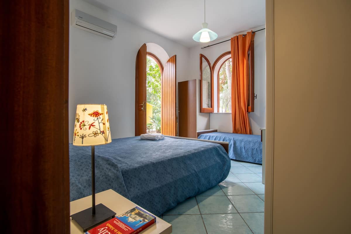 Un dormitorio con dos camas, una lámpara, un libro y una ventana con cortinas.